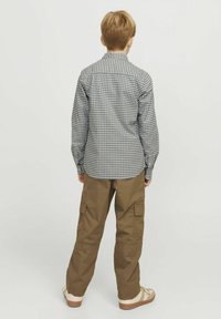 Camicia a maniche lunghe a scacchi grigi e bianchi abbinata a pantaloni cargo beige; la camicia ha polsini con bottoni, i pantaloni presentano tasche laterali.