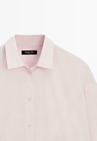 Světle růžová košile na zapínání s špičatým límečkem a třemi viditelnými knoflíky, zobrazující horní přední část a černou etiketu "Massimo Dutti" uvnitř límce.