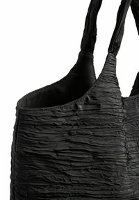 Svart axelväska med krinklad textur, mjukt material och två robusta handtag, designad med öppen topp för enkel åtkomst.