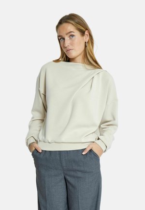 Sudadera de color beige claro con detalle de cuello doblado, textura suave, manga larga y dobladillo acanalado; combinada con pantalones grises de corte ajustado.