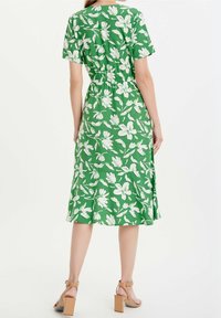 Grön klänning med vitt blommönster, kortärmad, med insvängd midja och utställd nederkant. Bärs med beige klacksandaler.