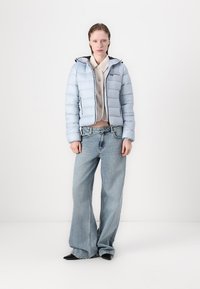 Lyseblå dunjakke med cropped design, svarte detaljer og hette; kombinert med løstsittende lyseblå jeans og svarte sko.