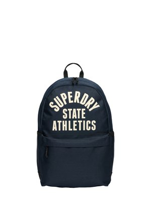 Navy blue fabric backpack with white "SUPERDRY STATE ATHLETICS" text, curved design, top handle, and front zippered pocket.
