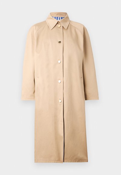 Manteau beige en tissu lisse, avec un col pointu, des boutons dorés et des poches latérales. Longueur genoux avec des manches longues.