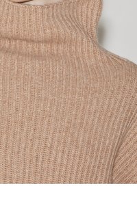 Beżowy sweter z prążkowanym golfem o miękkiej, dzianinowej fakturze, z wysokim kołnierzem i dopasowanym krojem.