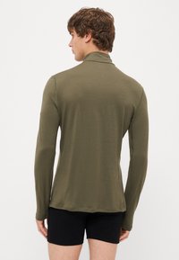 Olivovo zelená košeľa s dlhým rukávom, vysokým golierom a priliehavým strihom. Mäkká textura, slim fit a minimalistické švy.