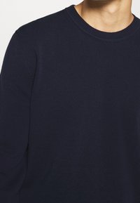 Marineblauer Pullover mit Rundhalsausschnitt aus weichem Strickstoff, mit langen Ärmeln und einem gerippten Halsausschnitt für zusätzliche Struktur.