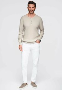 Maglietta a maniche lunghe beige a costine con tre bottoni, abbinata a pantaloni bianchi e scarpe in suede grigio chiaro. Design semplice con texture sottili.
