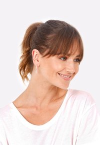 Orecchini a cerchio argento con un piccolo pendente a croce, indossati da un modello con capelli lunghi e texture morbida, che indossa una camicia bianca.
