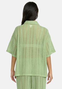 Maglione oversize di colore verde chiaro, con lavorazione a maglia aperta, collo a camicia e maniche corte, caratterizzato da una vestibilità rilassata e un sottile motivo testurizzato.