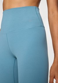 Aukšti liemeniu turkio spalvos leginsai, pagaminti iš elastinės medžiagos. Turintys subtilų Nike logotipą ir išsamią siuvinėjimo detalę palei siūles.