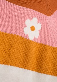 Gestrickter Pullover mit horizontalen Streifen in Orange, Pink und Weiß. Auffällige weiße Blumenstickerei auf dem pinken Streifen mit einem braunen Zentrum.