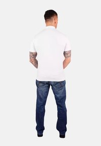 Maglietta bianca a maniche corte con colletto tondo, abbinata a jeans in denim blu. I jeans presentano un design sbiadito e dettagli di cucitura visibili.