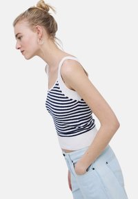 Top de punto a rayas en azul marino y blanco con un acabado texturizado. Presenta tirantes finos y un dobladillo acanalado. Combinado con pantalones de tiro alto en azul claro.