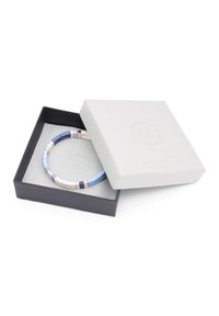 Pulsera de cuentas coloridas en tonos de azul, beige y acentos metálicos, exhibida dentro de una caja negra con una tapa blanca texturizada.