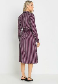 Abito lungo color bordeaux con strisce verticali bianche, maniche lunghe e vita con cintura. Presenta un colletto e una lunghezza fino al polpaccio. Tessuto liscio.