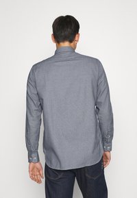 Camicia a maniche lunghe con bottoni in tessuto testurizzato blu scuro, con colletto classico e polsini bottonati, vista da dietro.