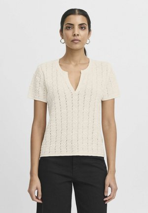Top corto a maniche corte in maglia color crema con scollo a V, caratterizzato da un motivo testurizzato e un design a maglia aperta. Indossato con pantaloni neri.