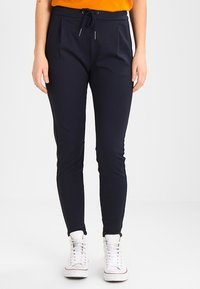 Mørkeblå joggebukser med elastisk midje og snøring, med sidelommer og slim fit. Kombinert med hvite joggesko.