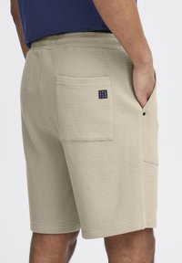 Shorts bej dintr-un material texturat, dotate cu un buzunar pe spate cu un mic eticheta logo și un elastic la talie pentru confort.