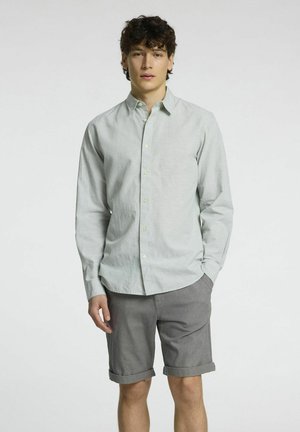 Chemise boutonnée vert clair à manches longues accompagnée de shorts gris. La chemise possède une texture douce et un motif tissé subtil.