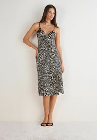 Zwart en beige luipaardprint midi-jurk met dunne bandjes, V-hals en een zijsplit, gemaakt van een lichtgewicht, glad materiaal. Zwarte sandaaltjes.