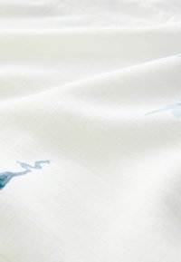 Hvidt stof med en glat tekstur, der har subtile blå broderede zigzag-mønstre, som skaber et elegant designdetalje.