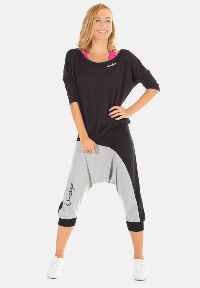Black and gray color-blocked high-waisted harem pants with side accents. Soft fabric, loose fit, rolled cuffs, and embroidered logo detail.