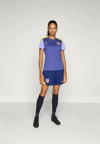 Purpursarkanais futbols krekls ar dzelteniem akcentiem un kluba logotipu, kombinēts ar tumši zilām biksēm un melniem zeķēm. Materiāls šķiet elpojošs un viegls.