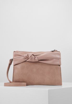 Miękka różowa prostokątna torebka z węzłowym akcentem z skóry i odpinanym paskiem na nadgarstek, umieszczona na białej powierzchni na jednolitym tle.