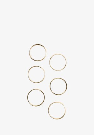 Sechs dünne goldene Ringe, angeordnet in zwei vertikalen Spalten auf weißem Hintergrund.