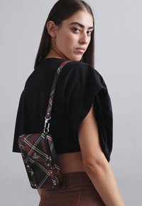 Mustra mustritask, millel on reguleeritav rihm, kui sellel on ristkülikuline kuju, läikiv riistvara ja punased, kollased ning rohelised aktsendid.