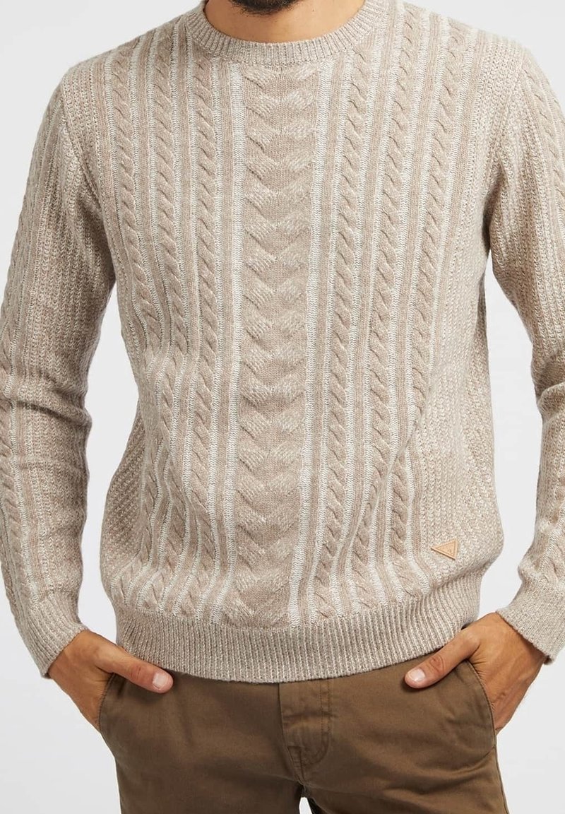 Beige-neulottu neulepusero, jossa on kuvioitu neulos, pyöreä kaula-aukko ja resorit hihansuissa. Alareunan vasemmassa reunassa pieni kolmionmuotoinen logo.