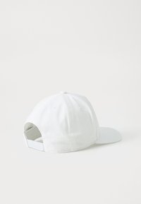 Hvit caps med rund krone, flat skjerm og justerbar stropp bak. Laget av stoff med glatt tekstur og minimalistisk design.