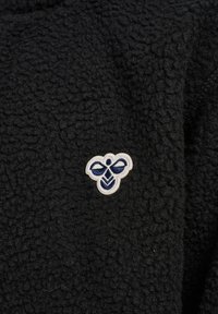 Sort tekstureret stof med en lille hvid og marineblå broderet bi-logo centreret på det.