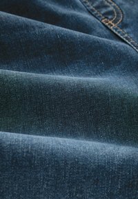 Sötétkék farmeranyag, sima textúrával, látható szövési mintákkal és finom fakulással, amely a minőségi farmerra jellemző.