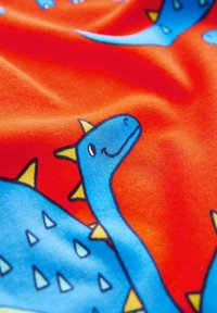 Niebieskie wzory dinozaurów z żółtymi kolcami na czerwonym tle; materiał jest miękki i gładki, z ilustracjami w stylu kreskówkowym.