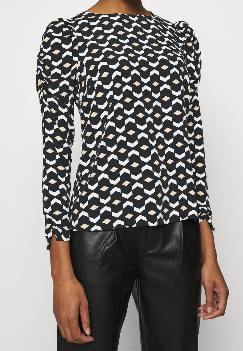 Černý top s dlouhým rukávem s geometrickým vzorem v bílé a béžové barvě. Tkanina vypadá hladce, s nařasenými detaily na ramenou.