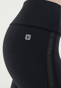 Leggings neri a vita alta in tessuto elasticizzato, con logo argentato e pannello laterale testurizzato con la scritta "FREDDY".