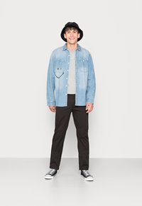 Light blue denim shirt with smiley face, gray t-shirt, black pants, and black bucket hat. Black and white sneakers.