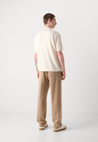 Polo shirt en tricot crème à manches courtes avec une coupe droite, associé à un pantalon beige à jambes larges. Texture lisse et détails de design simples.