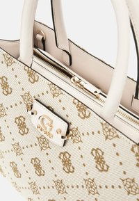 Beige textured handbag with gold logo accent, featuring a zippered closure and two handles, patterned with interlocking designs.