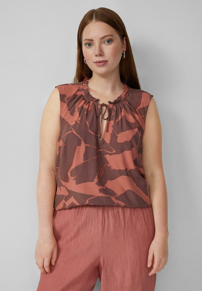 Top sans manches marron et rouille avec un col froncé, présentant un détail à nouer et des motifs abstraits, associé à un pantalon plissé rose pastel.