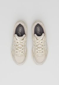 Beige sportskor med ovandel i mesh, gummisula och snörning. Har logodetalj på tungan och vadderad innersula.