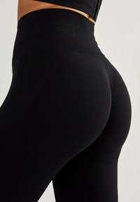Black high-waisted leggings with ribbed texture, featuring a logo on the waistband, designed for a fitted silhouette.
