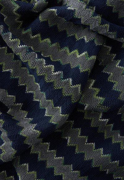 Tissu tricoté avec un motif en zigzag bleu marine, gris foncé et vert, montrant des plis et des détails de points texturés.