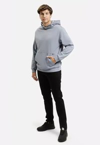 Jasnoniebieska bluza z kapturem wykonana z bawełny, z przednią kieszenią i regulowanym kapturem. Połączona z czarnymi spodniami i czarnymi trampkami.