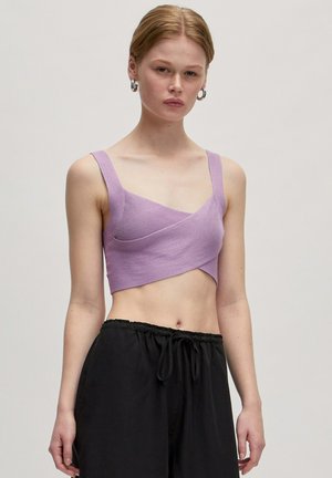 Lila Cropped-Top mit geripptem Textur und breiten Trägern, mit einem Wickeldesign. Kombiniert mit schwarzen Jogginghosen mit Kordelzug. Glatte Stoffoberfläche.