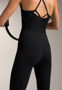 Top sport negru cu bretele încrucișate și leggings negri cu talie înaltă. Material moale, elastic, cu cusături minime și branding subtil.