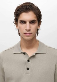 Polo shirt in light beige cotton knit with a collar, three black buttons, and ribbed texture, shown against a plain white background.